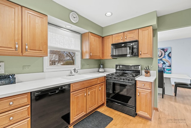 kitchen with black appliances, light countertops, light wood-type flooring, and a sink