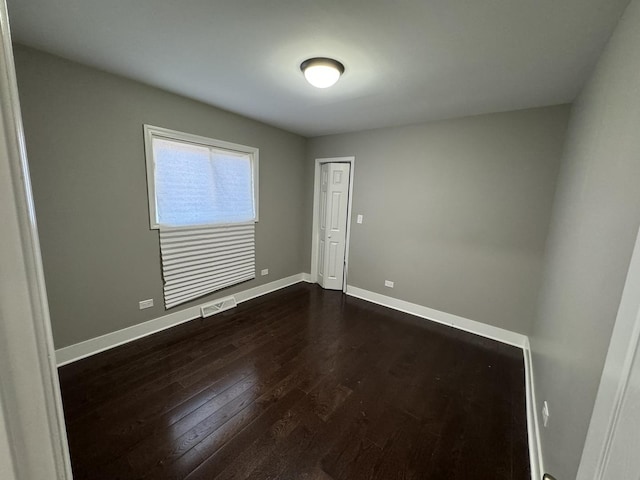 spare room with visible vents, baseboards, and dark wood-type flooring