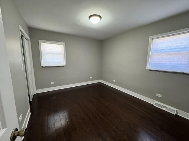 spare room with visible vents, a healthy amount of sunlight, dark wood-style floors, and baseboards