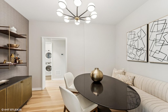 dining space featuring light wood-style flooring, visible vents, an inviting chandelier, stacked washer / dryer, and baseboards