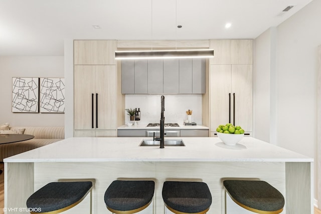 kitchen with recessed lighting, a kitchen breakfast bar, light stone counters, modern cabinets, and a center island with sink