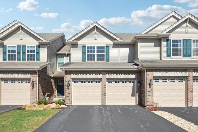 view of property featuring brick siding, an attached garage, a shingled roof, and driveway