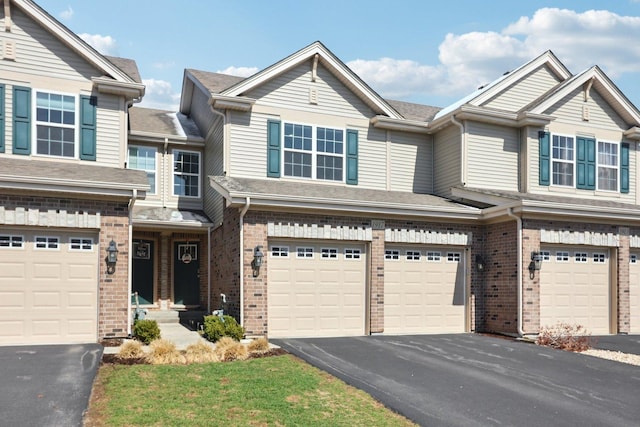 townhome / multi-family property with aphalt driveway, brick siding, and a garage