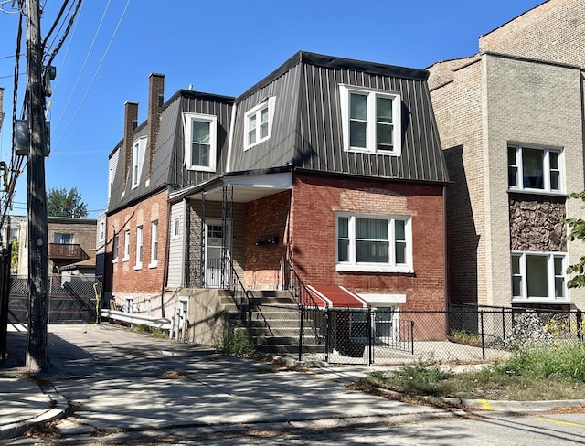 view of front of home featuring a fenced front yard, mansard roof, and brick siding