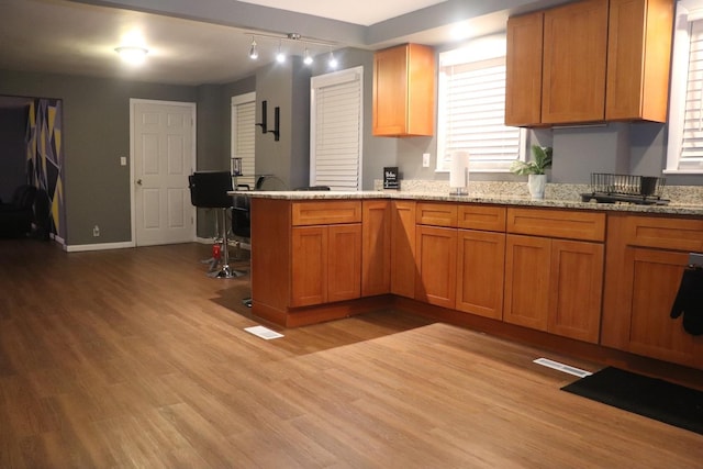 kitchen with baseboards, light stone countertops, light wood-type flooring, brown cabinets, and a peninsula