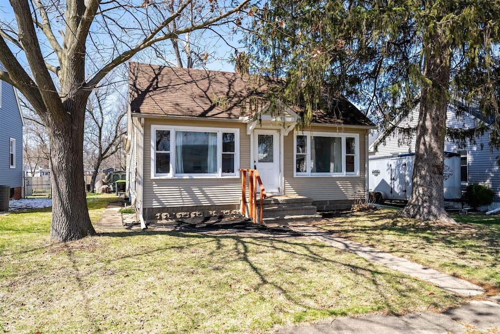 view of front facade with a front yard, central AC unit, and a shingled roof
