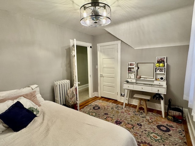 bedroom with a notable chandelier, radiator heating unit, wood finished floors, and baseboards
