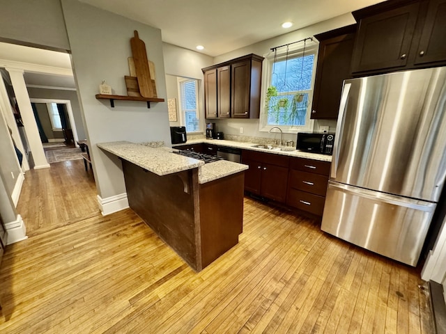 kitchen with dark brown cabinetry, light wood-style flooring, appliances with stainless steel finishes, a peninsula, and a sink