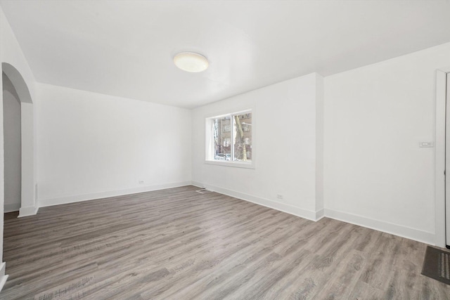 spare room with arched walkways, baseboards, visible vents, and wood finished floors