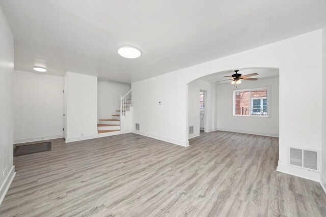 spare room with stairway, arched walkways, light wood-style floors, visible vents, and a ceiling fan