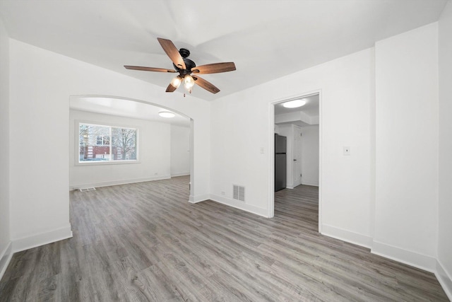 unfurnished room featuring a ceiling fan, arched walkways, wood finished floors, and visible vents