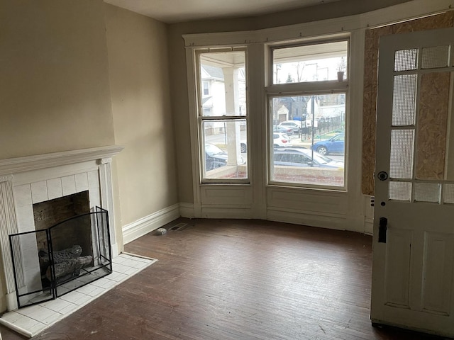 unfurnished living room with a tiled fireplace, baseboards, and wood finished floors