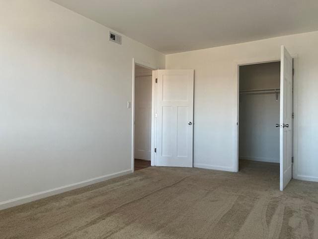 unfurnished bedroom featuring baseboards, a walk in closet, carpet flooring, and a closet