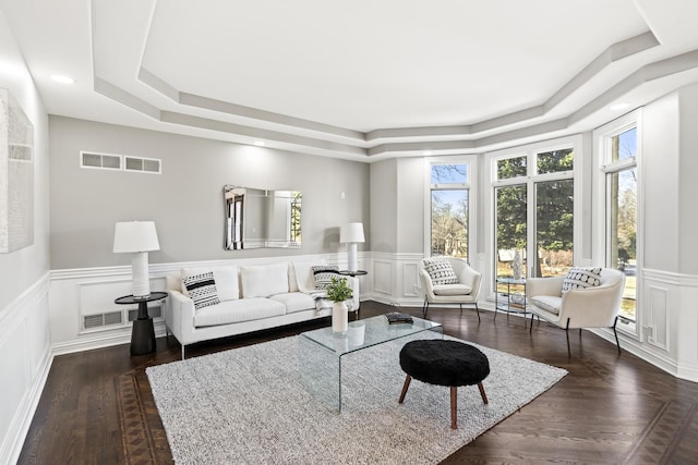 living area with dark wood-style floors, a decorative wall, a raised ceiling, and a wainscoted wall