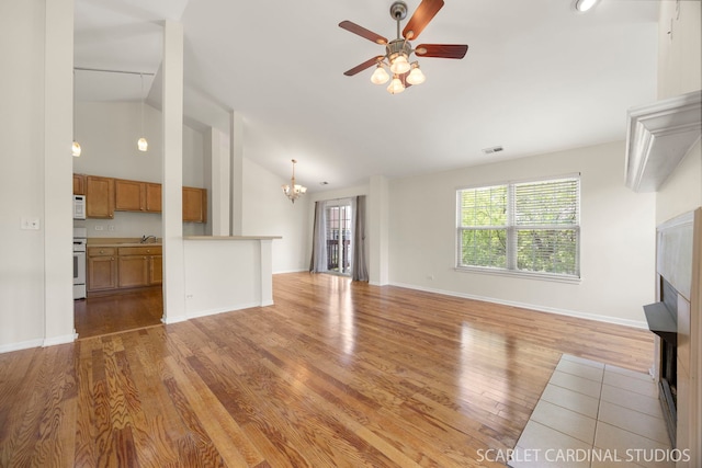 2319 Georgetown Ct, Aurora, IL 60503 - unfurnished living room featuring vaulted ceiling, a fireplace, light wood-style floors, ceiling fan, and a chandelier