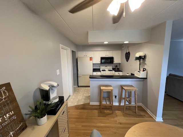 kitchen with black microwave, a peninsula, range with gas cooktop, dark countertops, and freestanding refrigerator