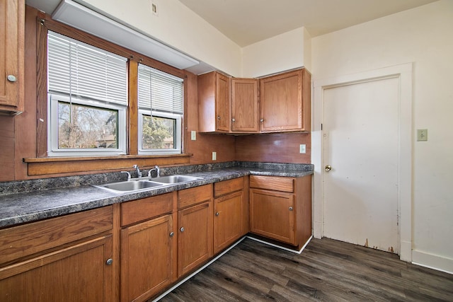 kitchen featuring dark countertops, brown cabinets, dark wood-style flooring, and a sink