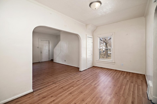 empty room with arched walkways, baseboards, a textured ceiling, and light wood-style floors