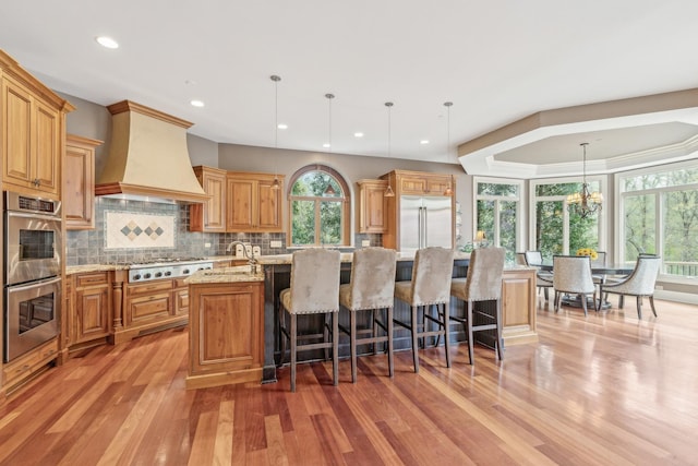 831 Alberosky Way, Batavia, IL 60510 - kitchen featuring appliances with stainless steel finishes, custom exhaust hood, a kitchen island with sink, light wood-type flooring, and backsplash