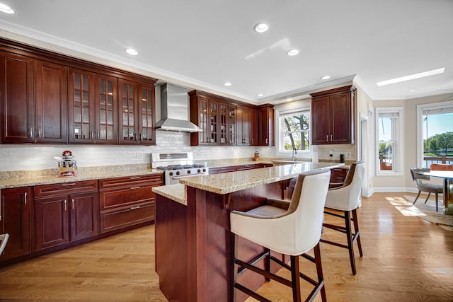 934 Robertson Rd, South Elgin, IL 60177 - kitchen with wall chimney range hood, gas range, a sink, a kitchen bar, and light wood-style floors