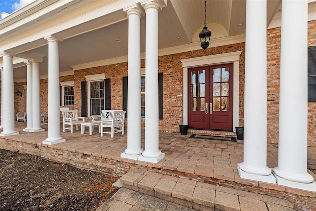 view of exterior entry with brick siding, a porch, and french doors