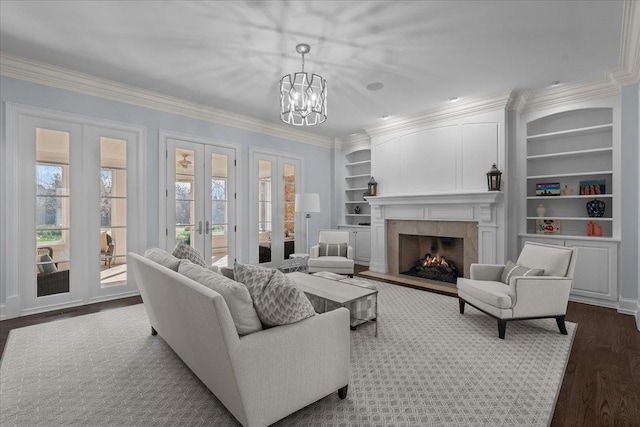 living room with dark wood-style flooring, a chandelier, crown molding, built in shelves, and french doors