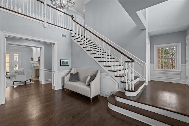 staircase with crown molding, wood finished floors, a decorative wall, visible vents, and an inviting chandelier