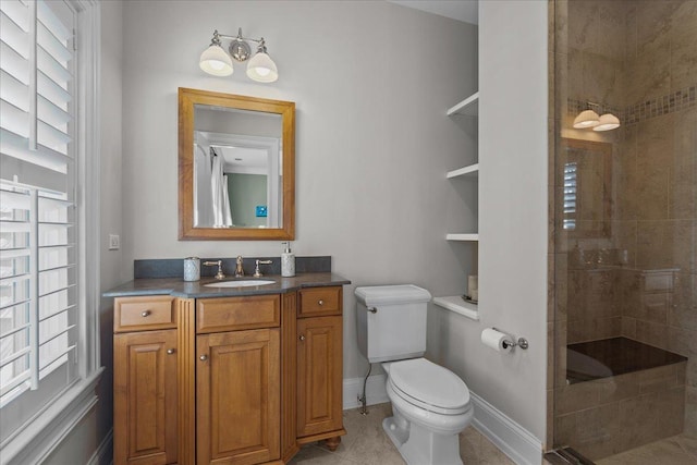 bathroom with tile patterned floors, a tile shower, toilet, vanity, and baseboards