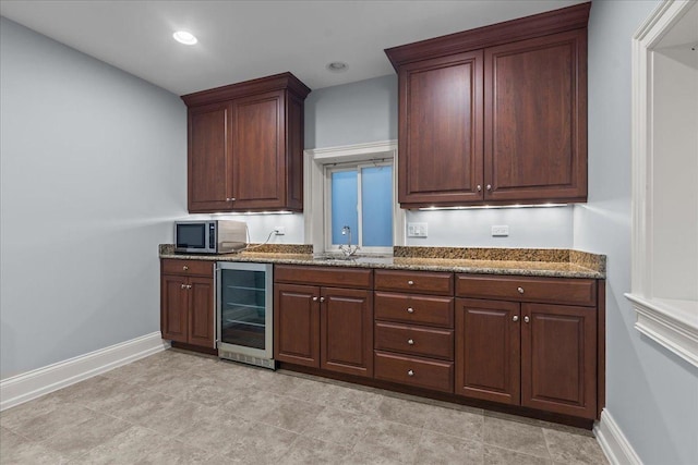 kitchen featuring stainless steel microwave, baseboards, dark stone counters, a sink, and beverage cooler