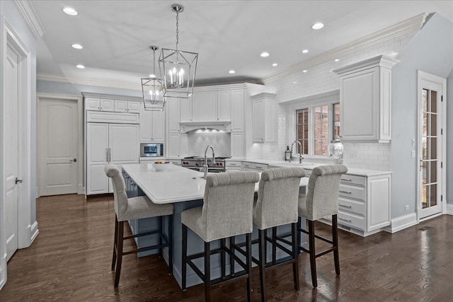 kitchen with a center island with sink, dark wood-style flooring, ornamental molding, and built in appliances