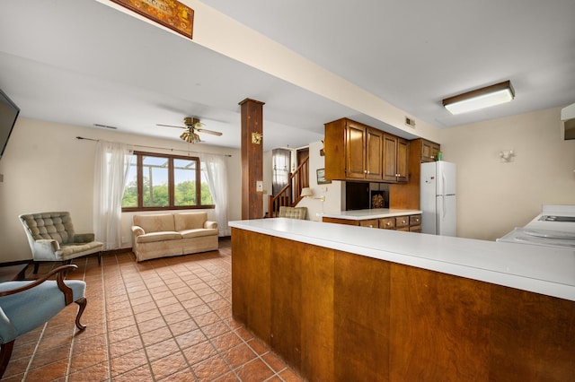 kitchen with brown cabinets, a ceiling fan, freestanding refrigerator, light countertops, and range