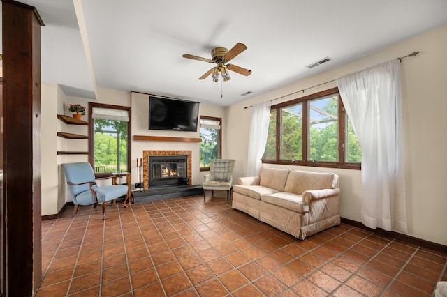 living room with a glass covered fireplace, visible vents, baseboards, and ceiling fan
