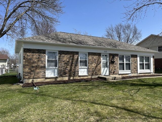 view of front of home with a front yard, brick siding, fence, and a shingled roof