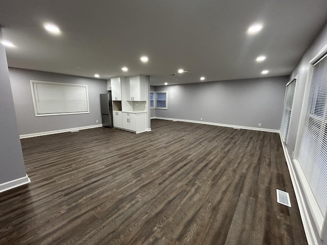 below grade area featuring dark wood-style flooring, baseboards, recessed lighting, freestanding refrigerator, and visible vents