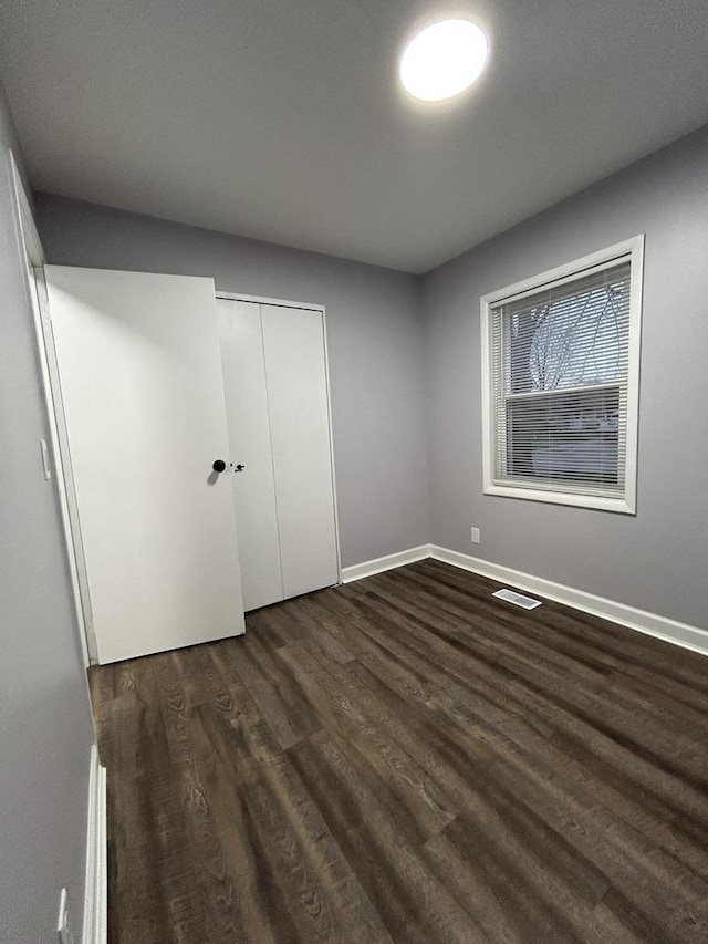 unfurnished bedroom featuring a closet, visible vents, baseboards, and dark wood finished floors