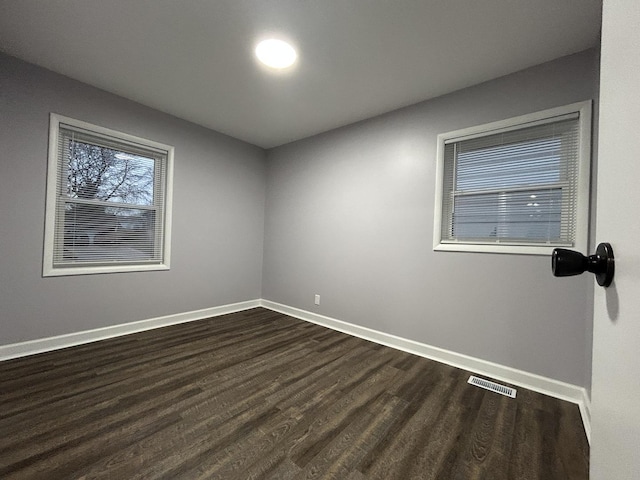 unfurnished room with visible vents, baseboards, and dark wood finished floors