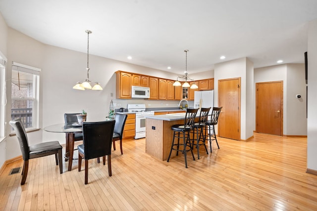 kitchen featuring white appliances, visible vents, a center island with sink, light wood finished floors, and a breakfast bar area