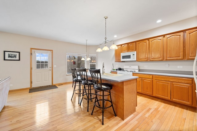 kitchen with white appliances, light wood-style flooring, a kitchen breakfast bar, and a kitchen island