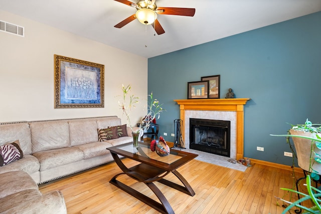 living room featuring visible vents, baseboards, ceiling fan, a fireplace, and wood-type flooring