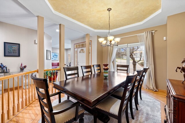 dining space with baseboards, a raised ceiling, a chandelier, and light wood finished floors