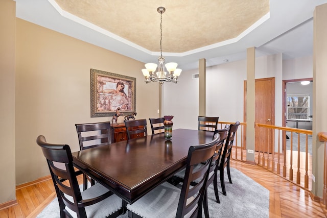 dining area with a tray ceiling, baseboards, light wood-type flooring, and an inviting chandelier