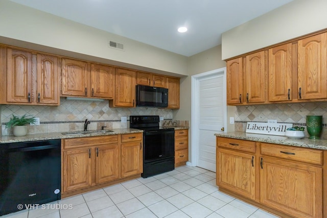kitchen featuring visible vents, light stone countertops, a sink, black appliances, and brown cabinetry