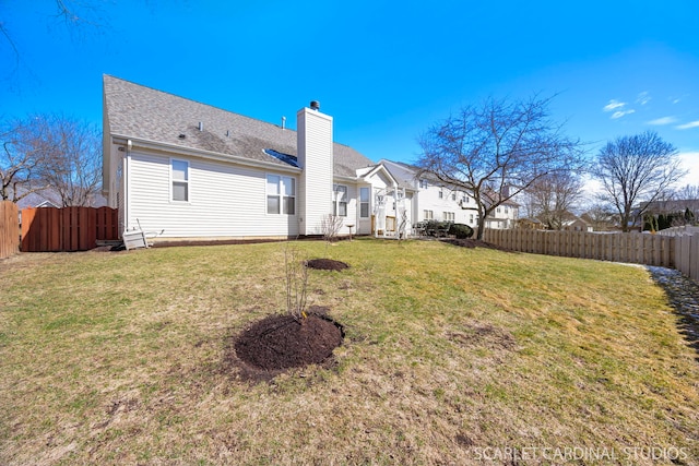 rear view of house featuring a lawn, a chimney, a shingled roof, and a fenced backyard