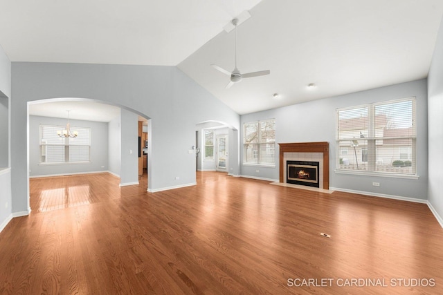 unfurnished living room featuring a fireplace with flush hearth, arched walkways, wood finished floors, and ceiling fan with notable chandelier
