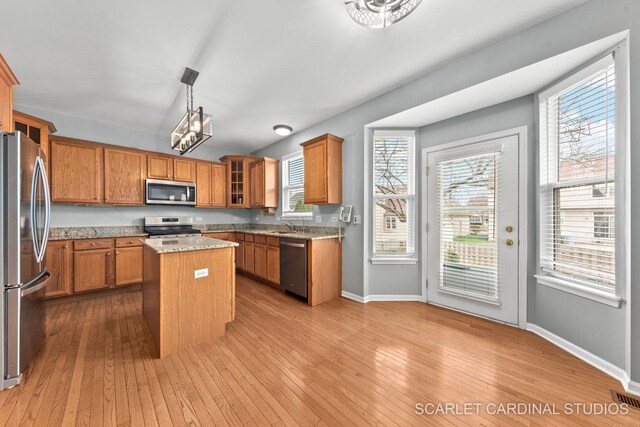 kitchen featuring wood-type flooring, a center island, appliances with stainless steel finishes, and brown cabinetry