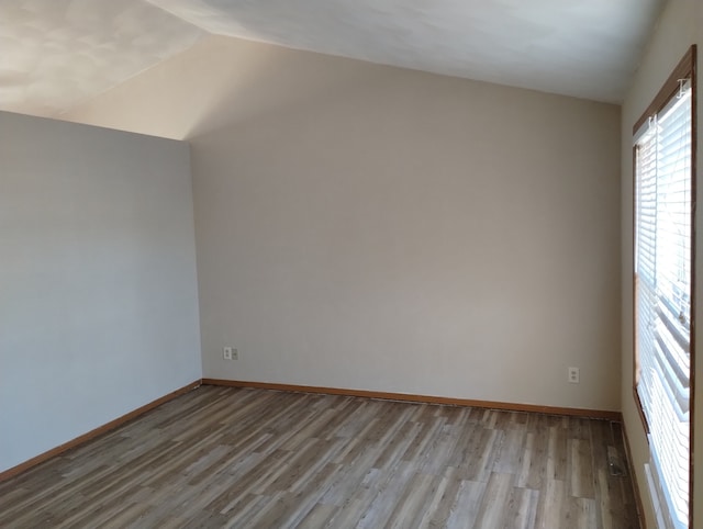 empty room with baseboards, vaulted ceiling, and wood finished floors