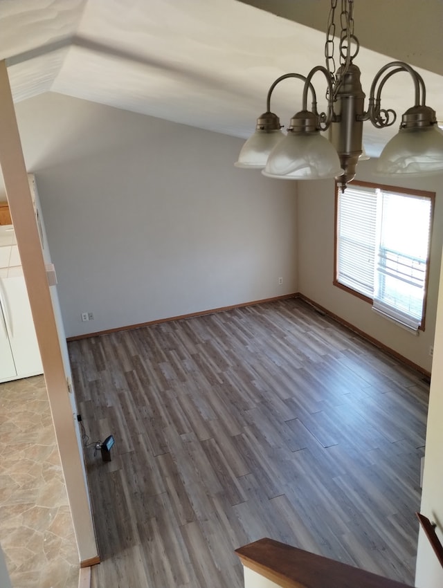 unfurnished dining area with baseboards, lofted ceiling, wood finished floors, and a chandelier