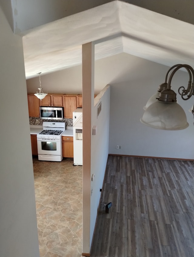 kitchen featuring white range with gas stovetop, stainless steel microwave, vaulted ceiling, backsplash, and fridge
