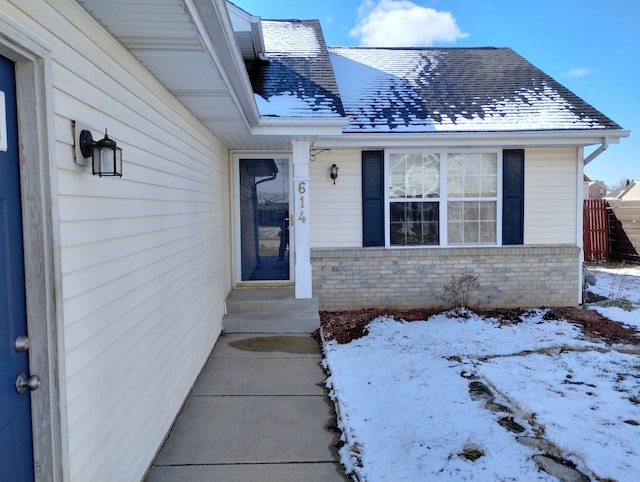 snow covered property entrance with brick siding and a shingled roof