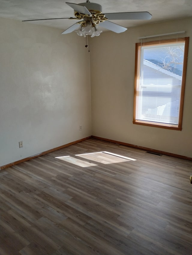 empty room with baseboards, visible vents, ceiling fan, and wood finished floors